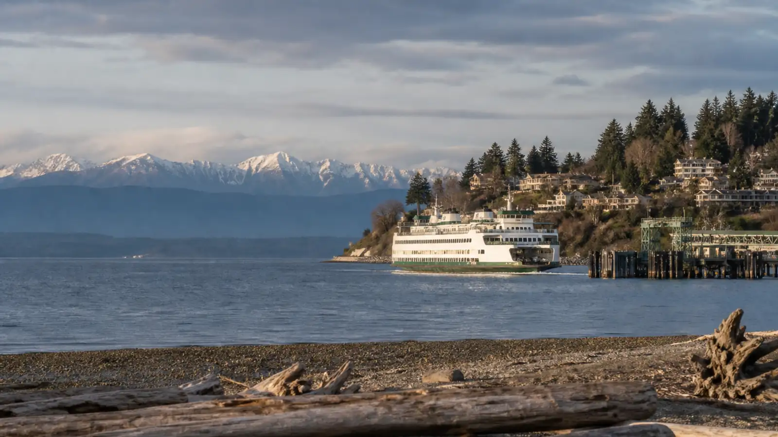 A ferry departing a small-town terminal with jagged mountains beyond the water