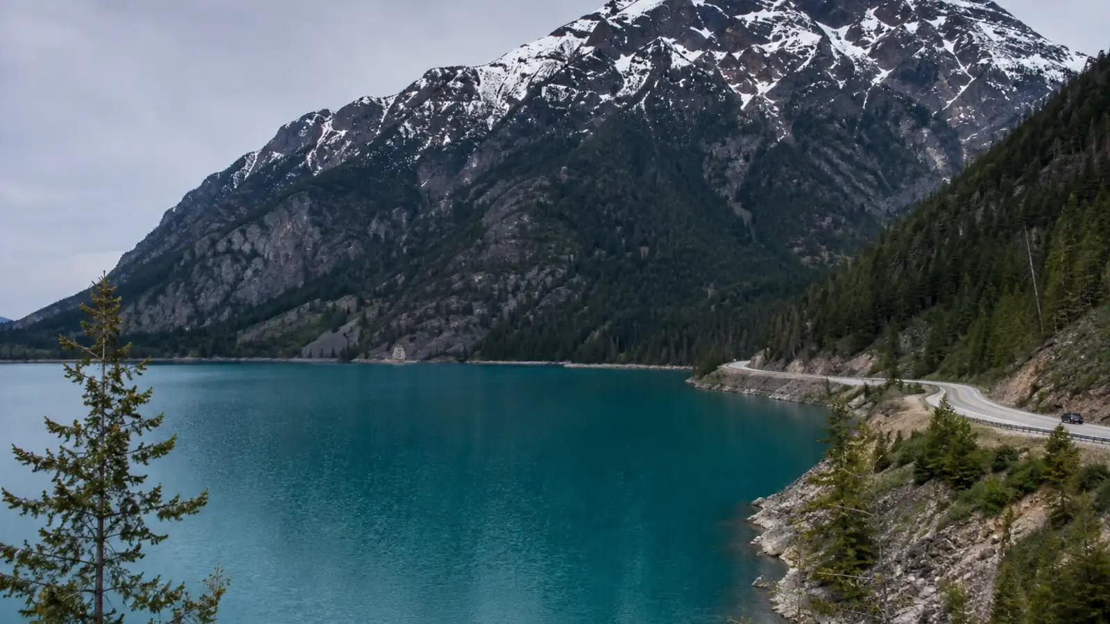 A turquoise glacial lake below steep forested mountains