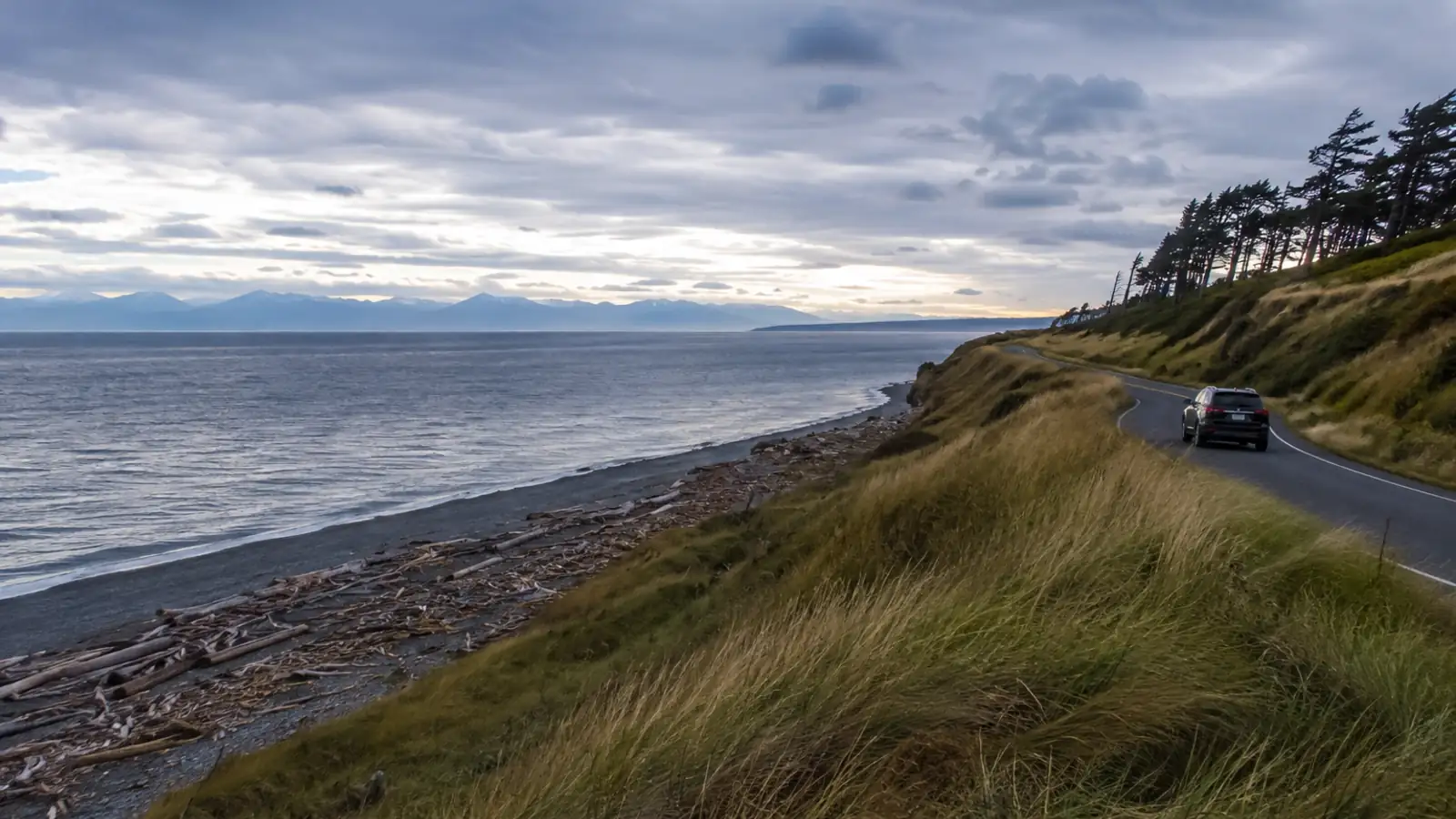 A bluff-top road above a driftwood beach with the strait beyond