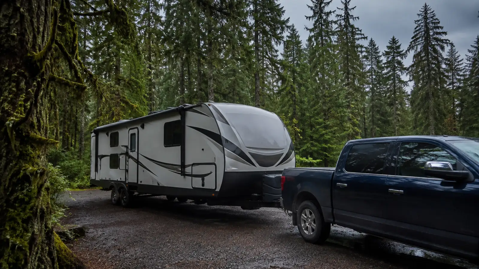 A travel trailer hitched to a pickup truck at a forested campsite